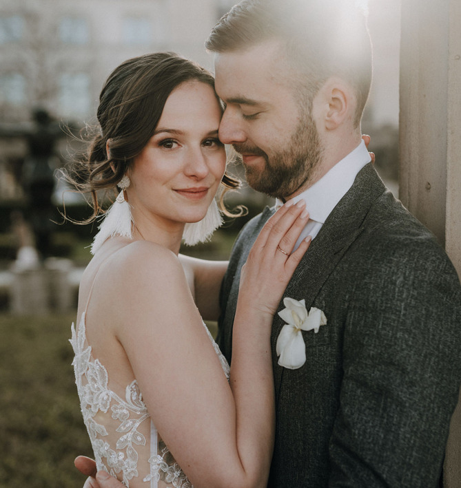 die Braut im romantischen Boho-Look, hat eine Hand auf den Bräutigam gelegt, der sie liebevoll ansieht und eng an sich zieht