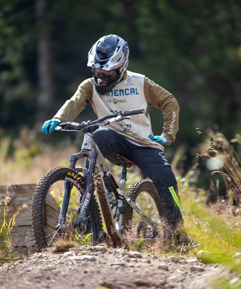 Mountain biker in a full-face helmet and jersey resting on a forest trail with his downhill bike.
