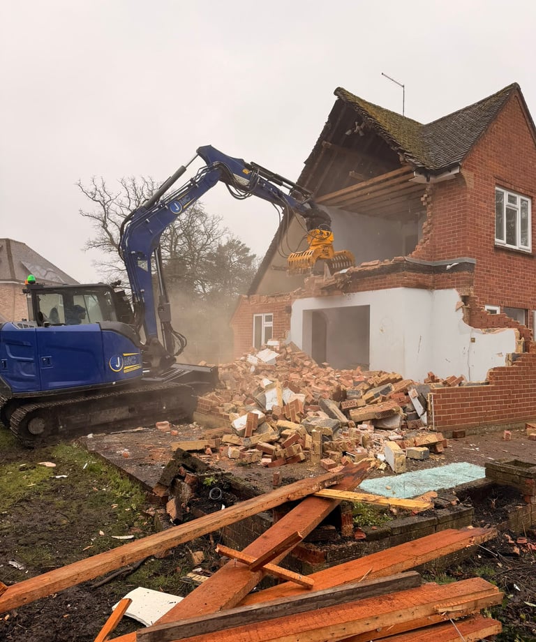 A blue hydraulic excavator demolishes a brick residential house during a site clearance and renovation project.