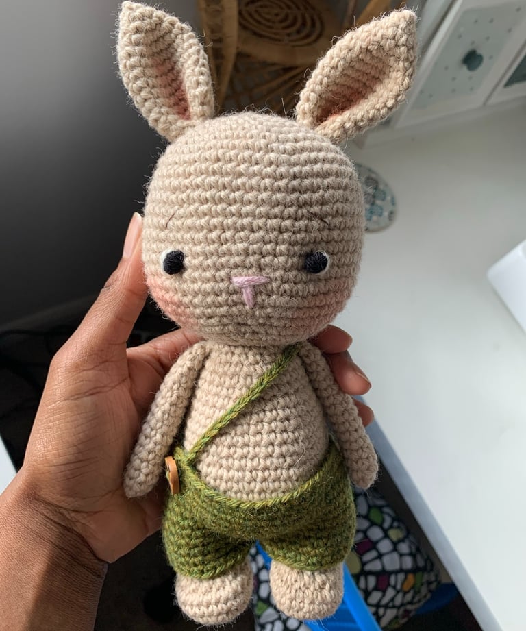 a person holding a crochet bunny rabbit wearing overalls