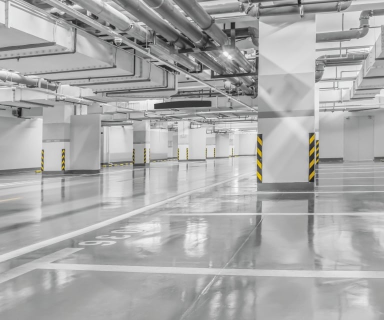 Jasny, pusty parking podziemny z gładką, odbijającą światło posadzką i filarami.