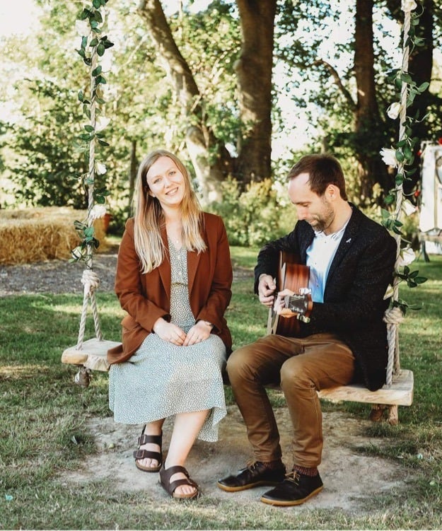 a man and woman sitting on a swing with a guitar at wedding
