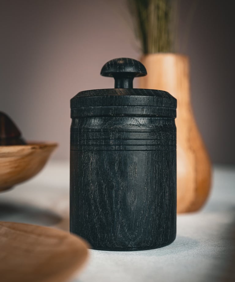 Pot à épices en bois foncé artisanal avec couvercle sculpté, posé sur une table. Sa texture naturell