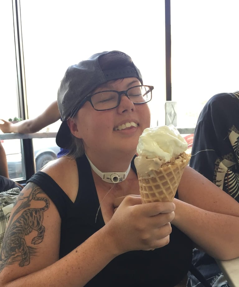 Photo of Stacey enjoying a ice cream cone. Her head is back with a big smile, her tattoo is visible
