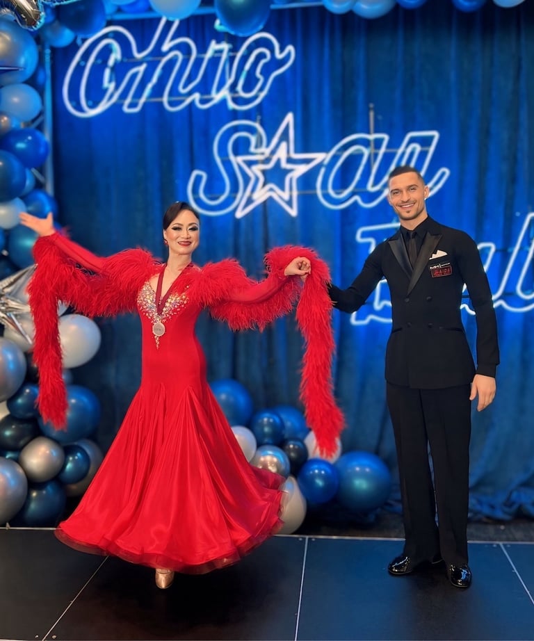 A ballroom couple performing a bow, with the man in a black suit presenting the woman in a red dress