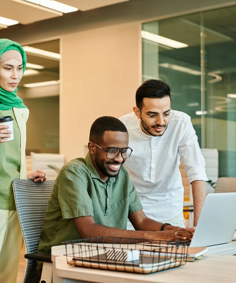 one male colleague seated at laptop and female and male colleague look at screen with him.