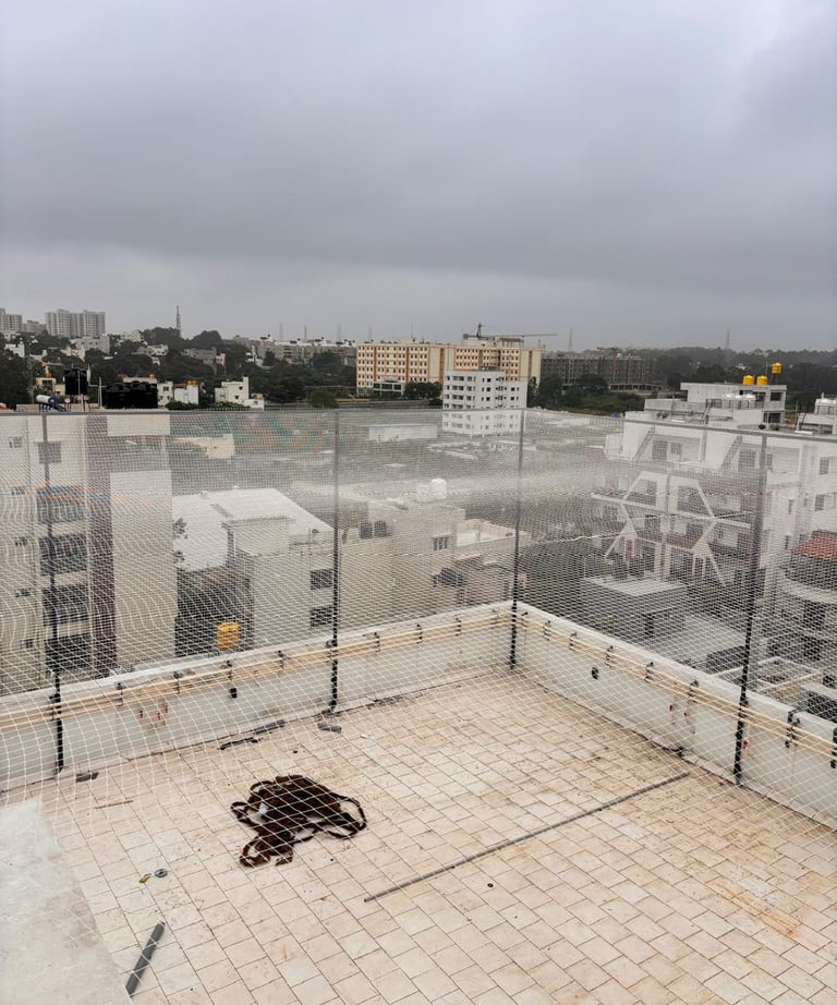 Wide shot of a residential balcony fully covered with a pigeon net, sunlight filtering through.