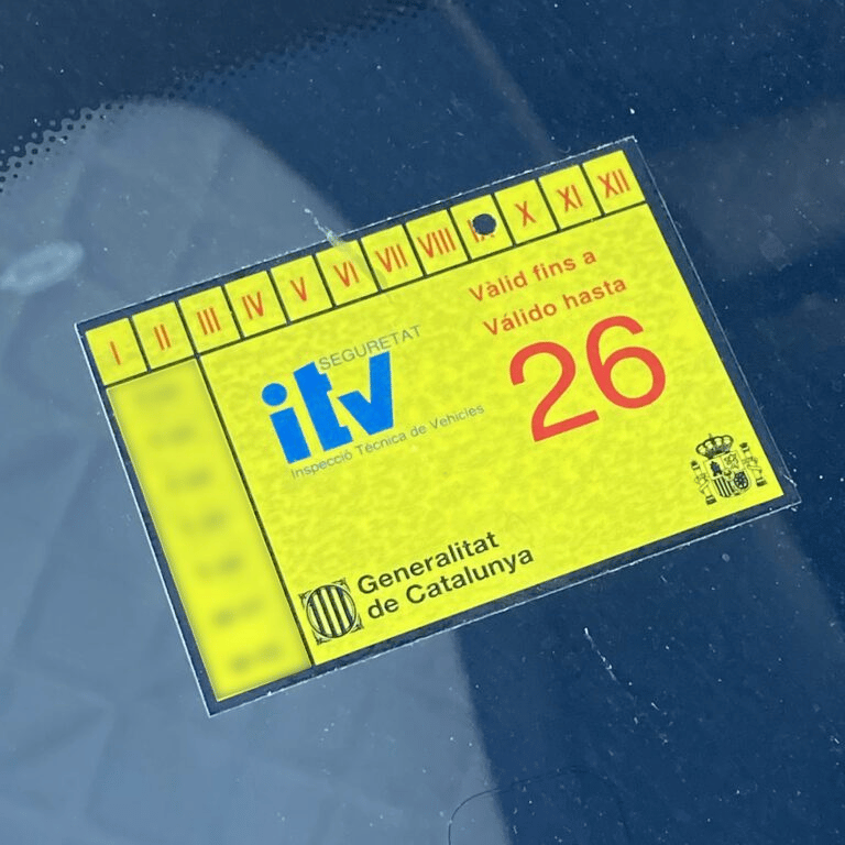 Yellow Spanish ITV inspection sticker on a car windshield valid until 2026 in Catalonia.