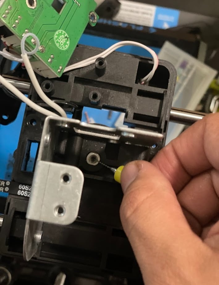 Hand clearing a clogged 3D printer nozzle using a fine needle cleaning tool.