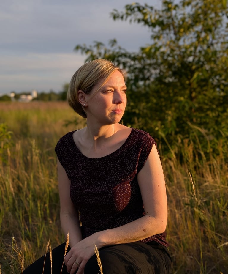 Grabrednerin kniet auf einer Wiese und schaut in den Sonnenuntergang in Falkensee