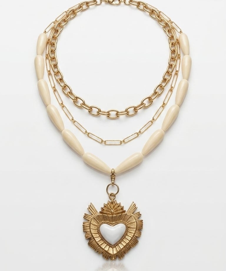 Layered gold chain necklace featuring ivory beads and a sacred heart pendant with white enamel.