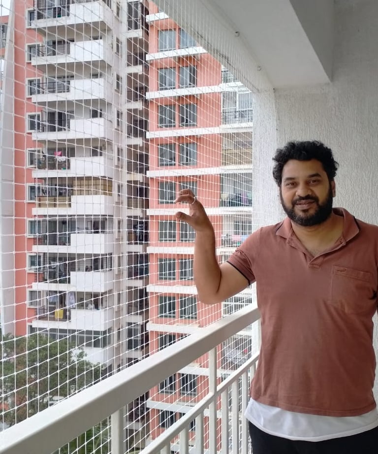 Technician carefully fitting a safety net on a balcony railing with tools in hand.