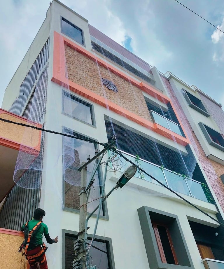 Technician carefully fitting a pigeon safety net on a high-rise apartment window in Mumbai.