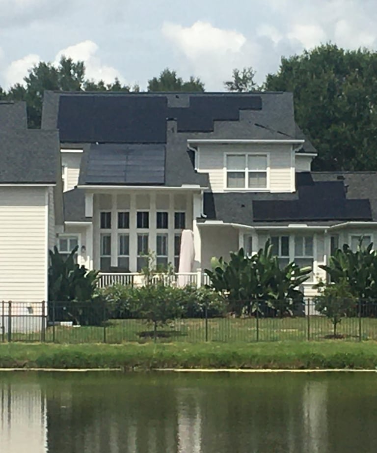 Modern suburban home with residential solar panels installed on a shingle roof near a lakeside.