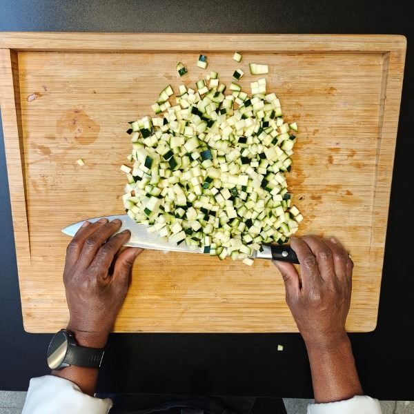 Chef Viviane's hands chopping courgette into fine dice with a chef's knife, top-down view