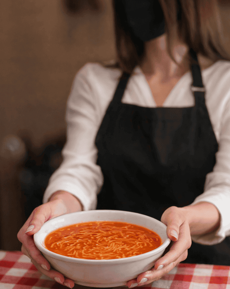 Mujer entregando plato de sopa aguada