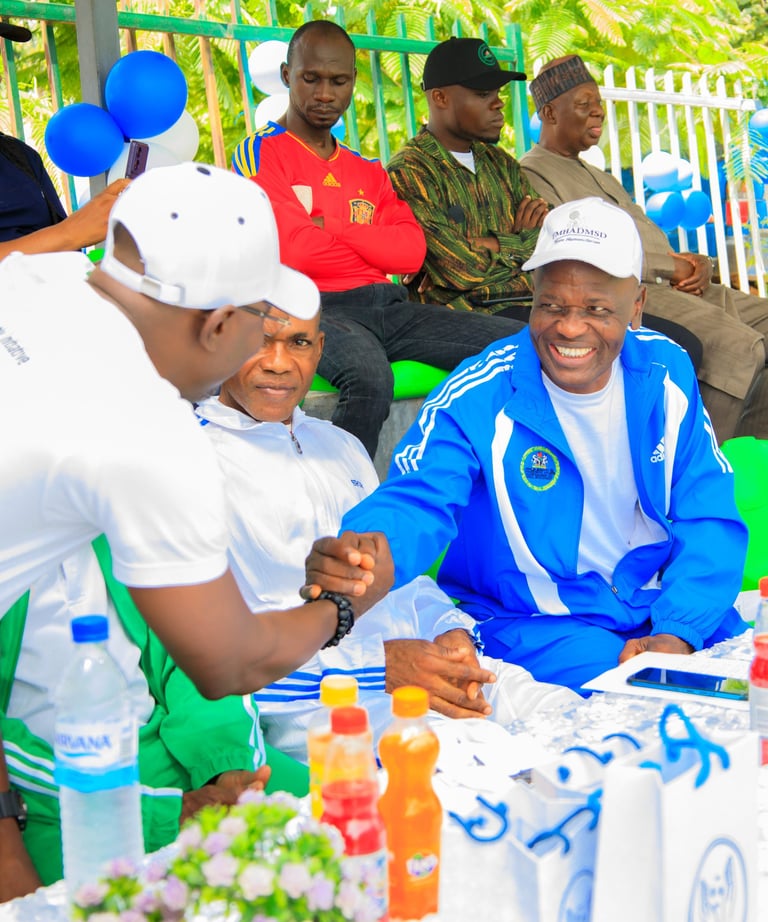 a man in a blue jacket and white shirt sitting at a table with balloons