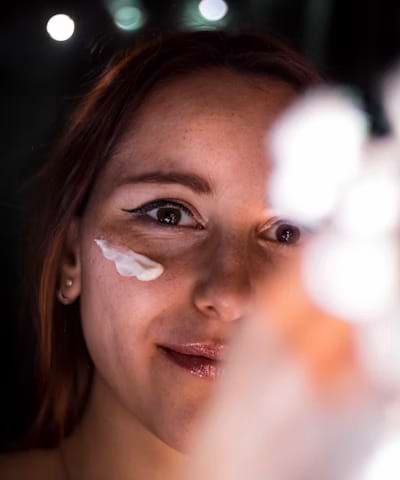 Woman smiling while applying face cream under her eye as part of a skincare routine.