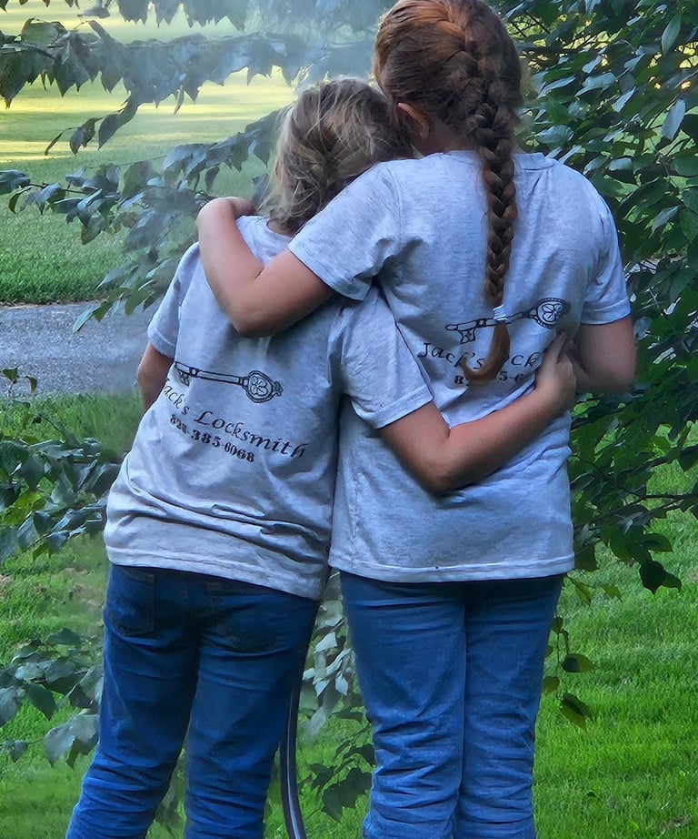 Two daughters hugging outdoors while wearing matching locksmith work shirts