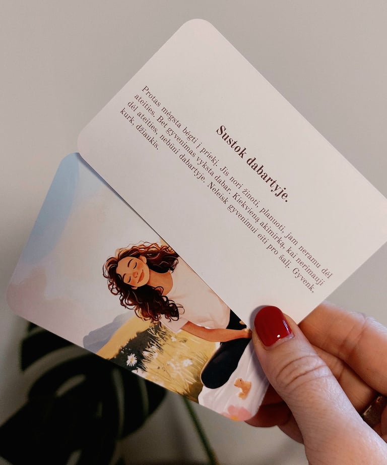 Psichologinės kortelės mamai su tekstu "sustok dabartyje" laikomos rankoje.