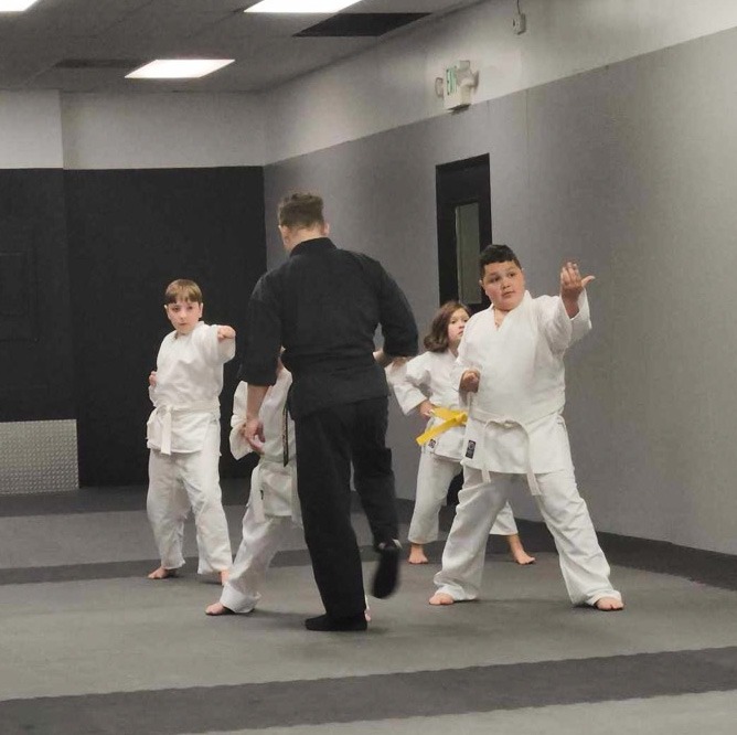 Children in white karate gi practice martial arts strikes during a youth training class.