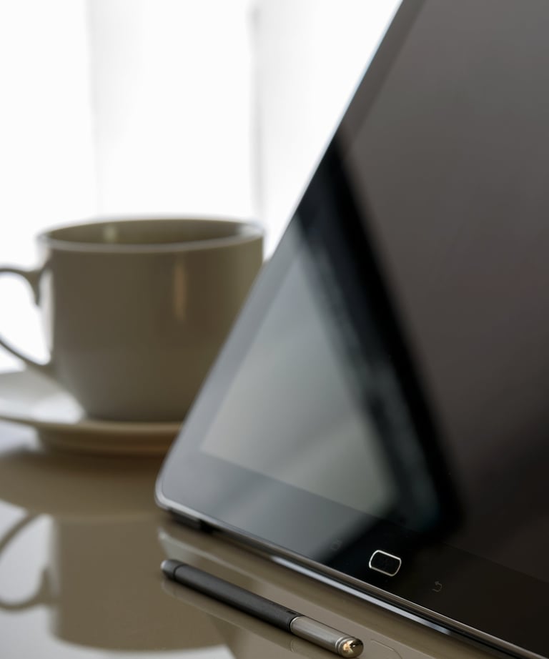 um-tablet-desligado-em-cima-de-uma-mesa-e-uma-xícara-de-café-ao-fundo