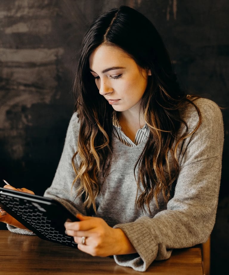 a woman sitting at a table with a laptop and a tablet