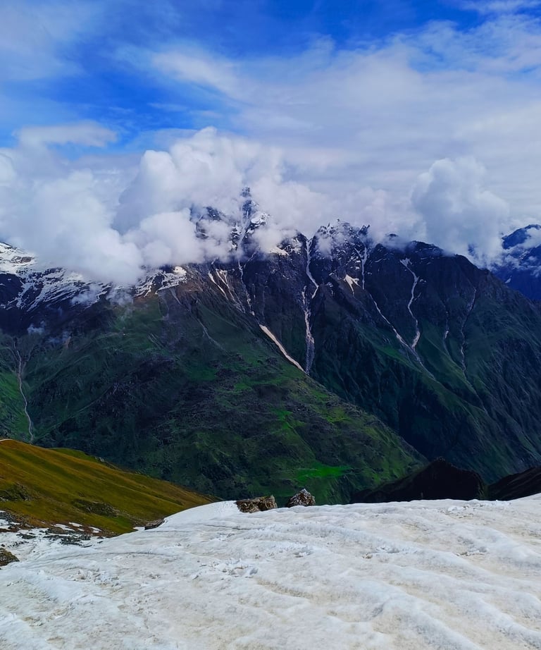 Snowy peaks with clouds over green valleys.