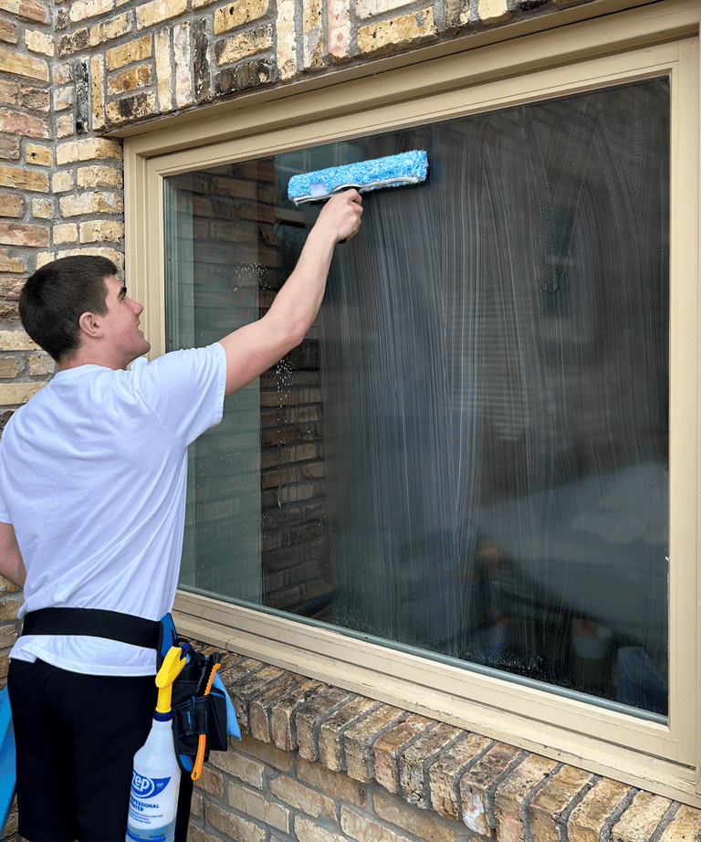 Logan Fotsch is using cleaning brush to wash a large window.