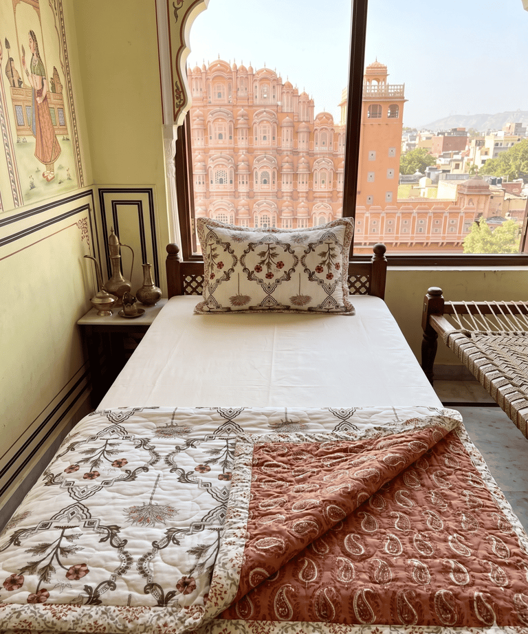 A boutique hotel bedroom in Jaipur featuring a view of the Hawa Mahal palace from the window.