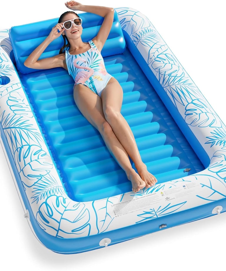 A woman relaxes on a blue inflatable tanning pool with tropical leaf patterns for summer backyard fun.