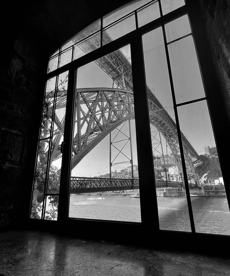 Black and white view of the Dom Luis I Bridge in Porto seen through a stone window.