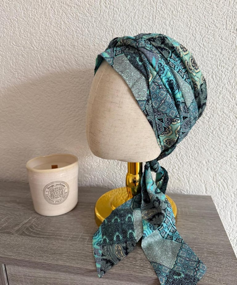 Turban en tissu vert et bleu à motifs, présenté sur un présentoir de tête.