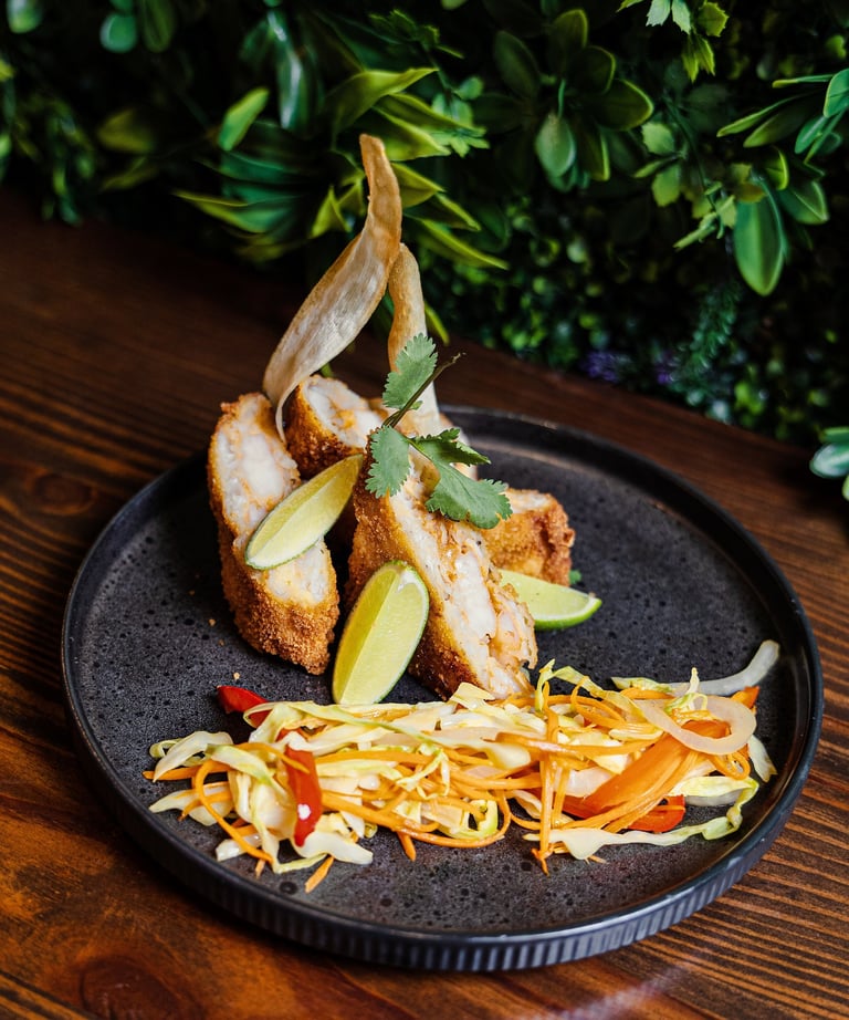 Crispy breaded shrimp appetizer served with fresh lime wedges and a side of vegetable slaw on a dark plate.