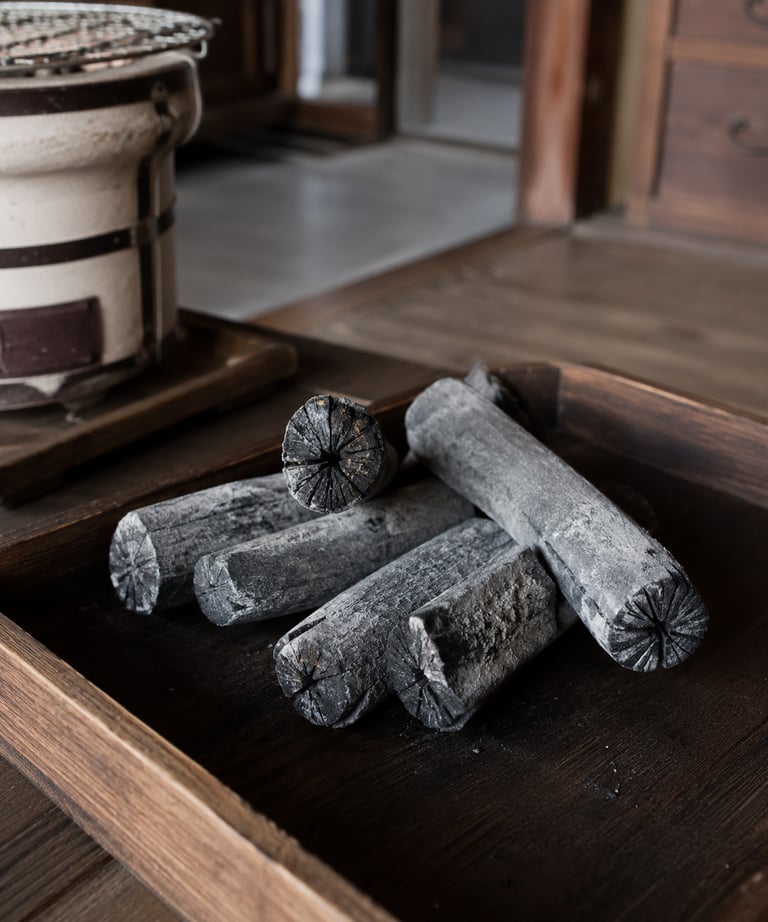 Traditional binchotan white charcoal sticks on a wooden tray for Japanese konro grill cooking.