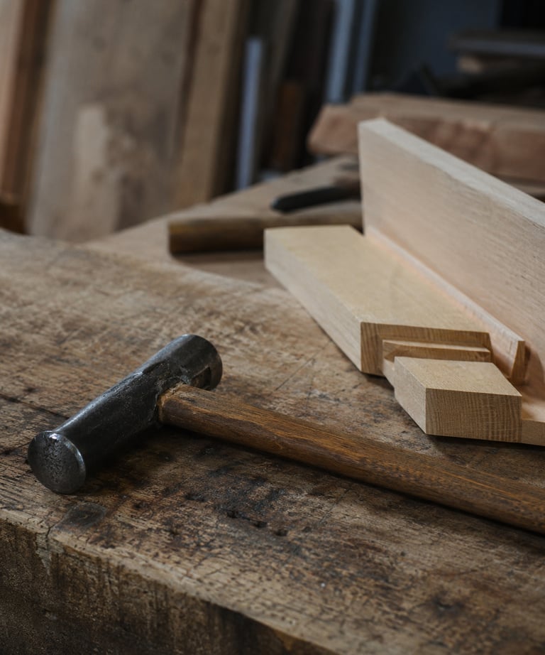 Vintage metal hammer laying on a rustic wooden workbench in a carpentry workshop.