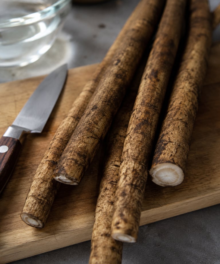 Fresh raw burdock root on a wooden cutting board with a paring knife for healthy cooking.
