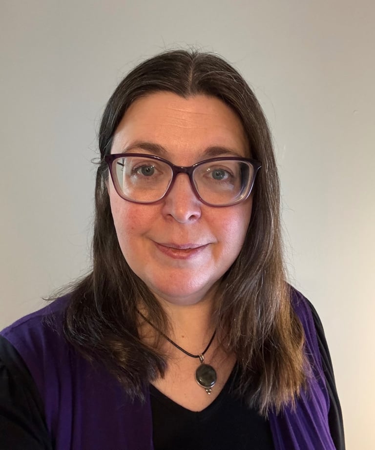 A woman with brown hair wearing glasses and smiling.
