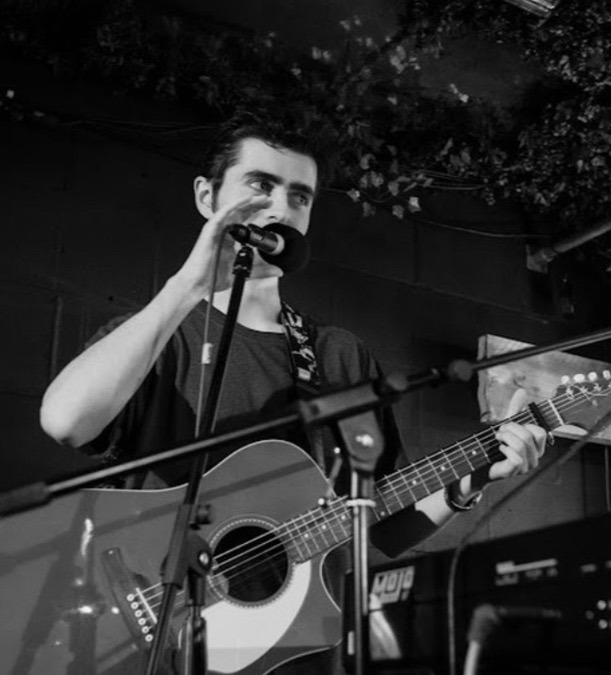 Black and white photo of Brighton musician Olly Williams singing and playing guitar