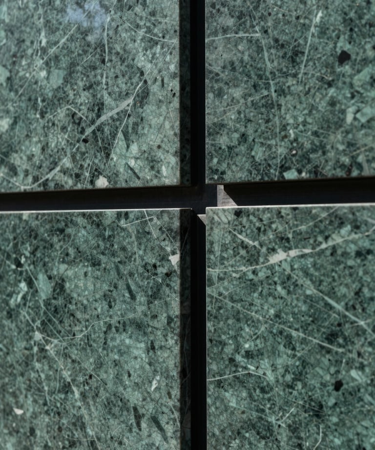 Close-up architectural detail of a deep-green marble wall panel meeting a polished black steel frame, precise joinery visible, cool diffused north light, no people, abstract material geometry