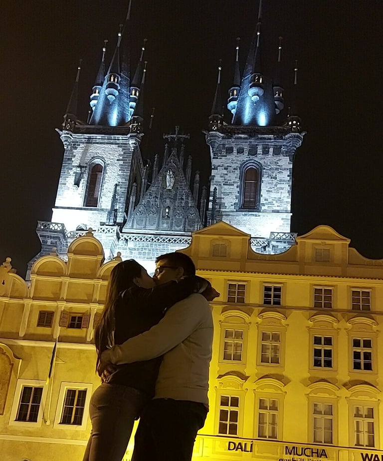 Pareja abrazándose frente a la Iglesia de Týn iluminada por la noche en Praga.