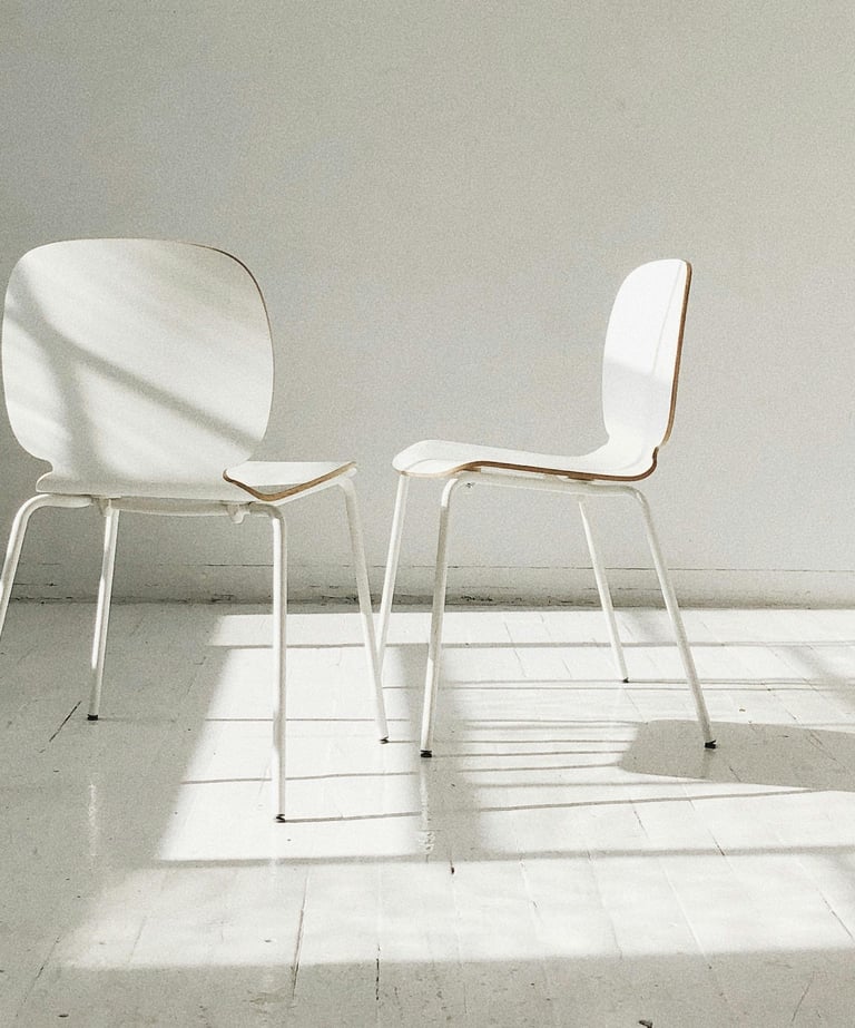 Twee witte stoelen schuin tegenover elkaar met een open ruimte ertussen, symbool voor oudercontact 