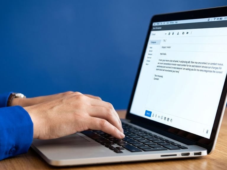 A person typing on a laptop keyboard to compose a professional email for business communication.
