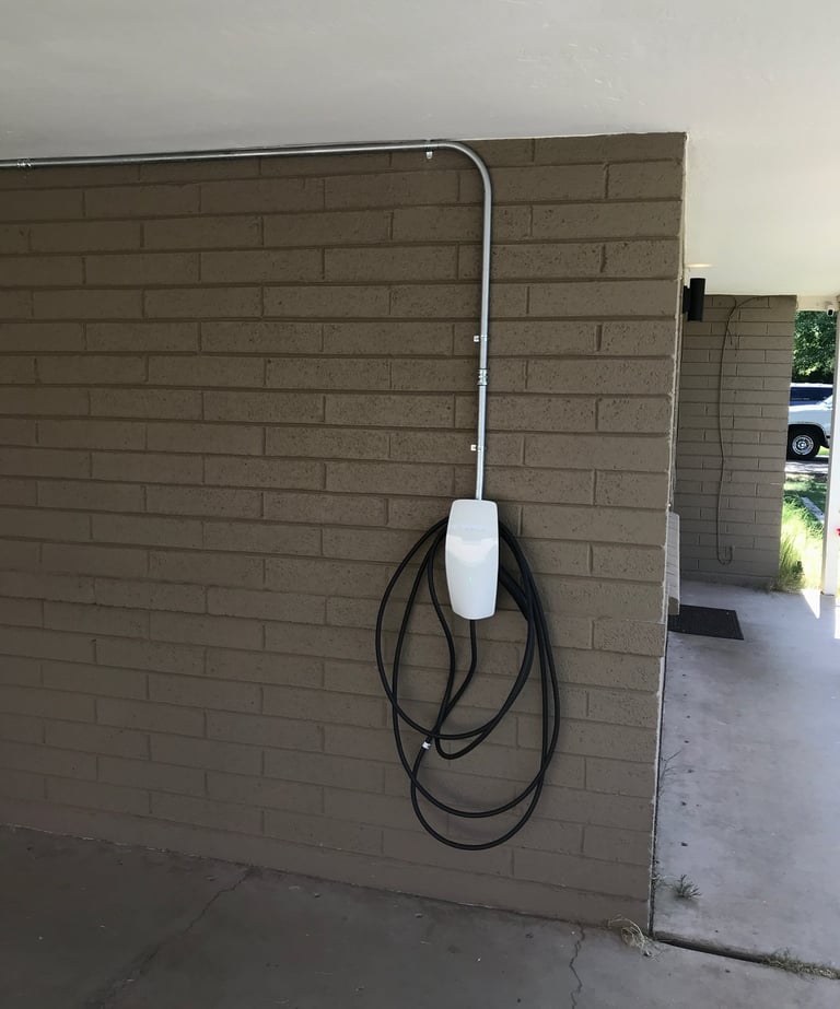 A white Tesla Wall Connector electric vehicle home charging station mounted on a brown brick wall.