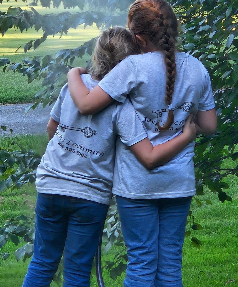 Two daughters in Jack's Locksmith t-shirts hugging outdoors in Spruce Pine NC