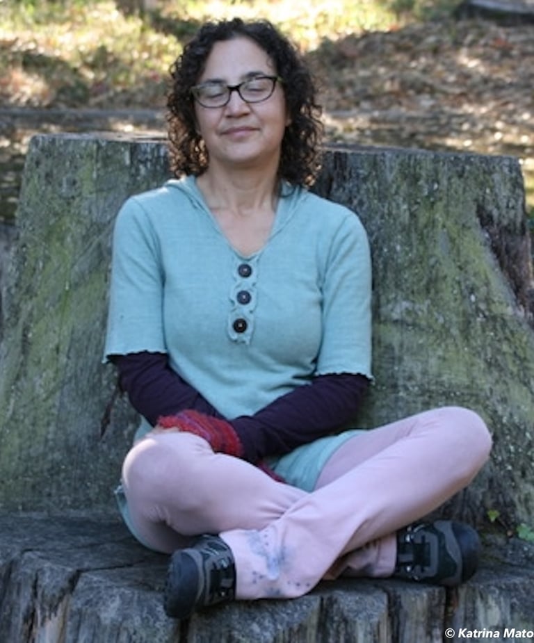 Katrina sitting on a tree stump with eyes closed smiling