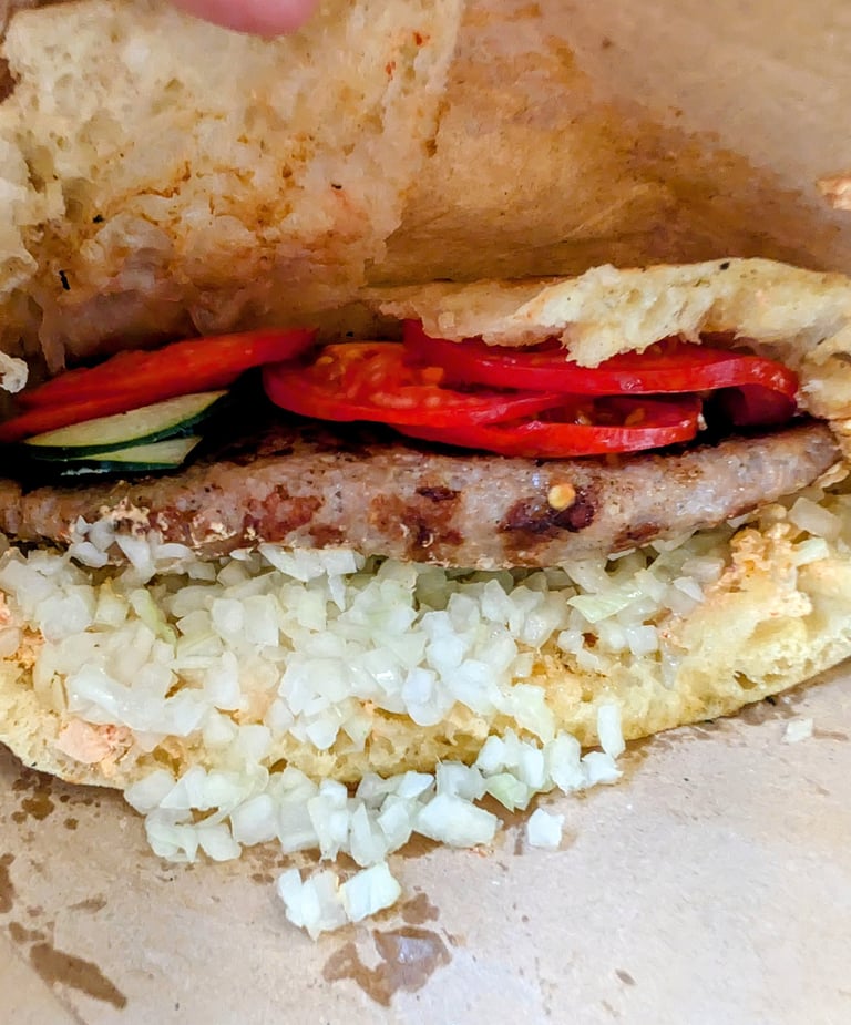 Close-up of a Serbian pljeskavica patty in lepinja bread with onions and tomatoes.