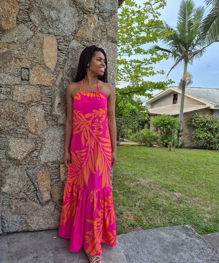 Mulher em pé usando um vestido com babado franzido, estampado nas cores rosa e laranja