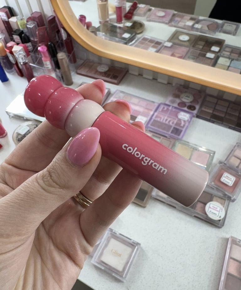 Hand holding a Colorgram pink gradient lip tint in a vanity filled with Korean beauty makeup palettes.