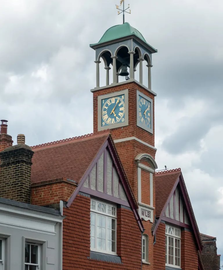 Historic red brick clock tower with a green dome and gold Roman numerals under a cloudy sky.
